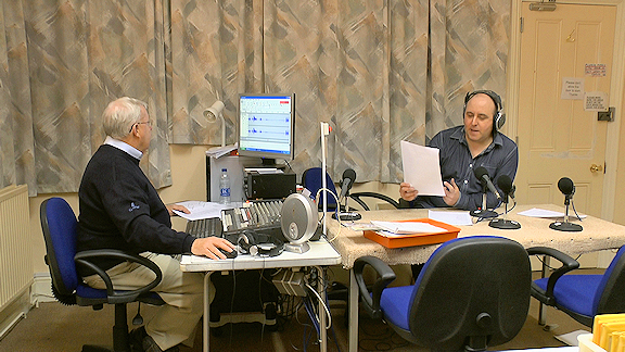 Recordist at computer and person speaking into a microphone behind